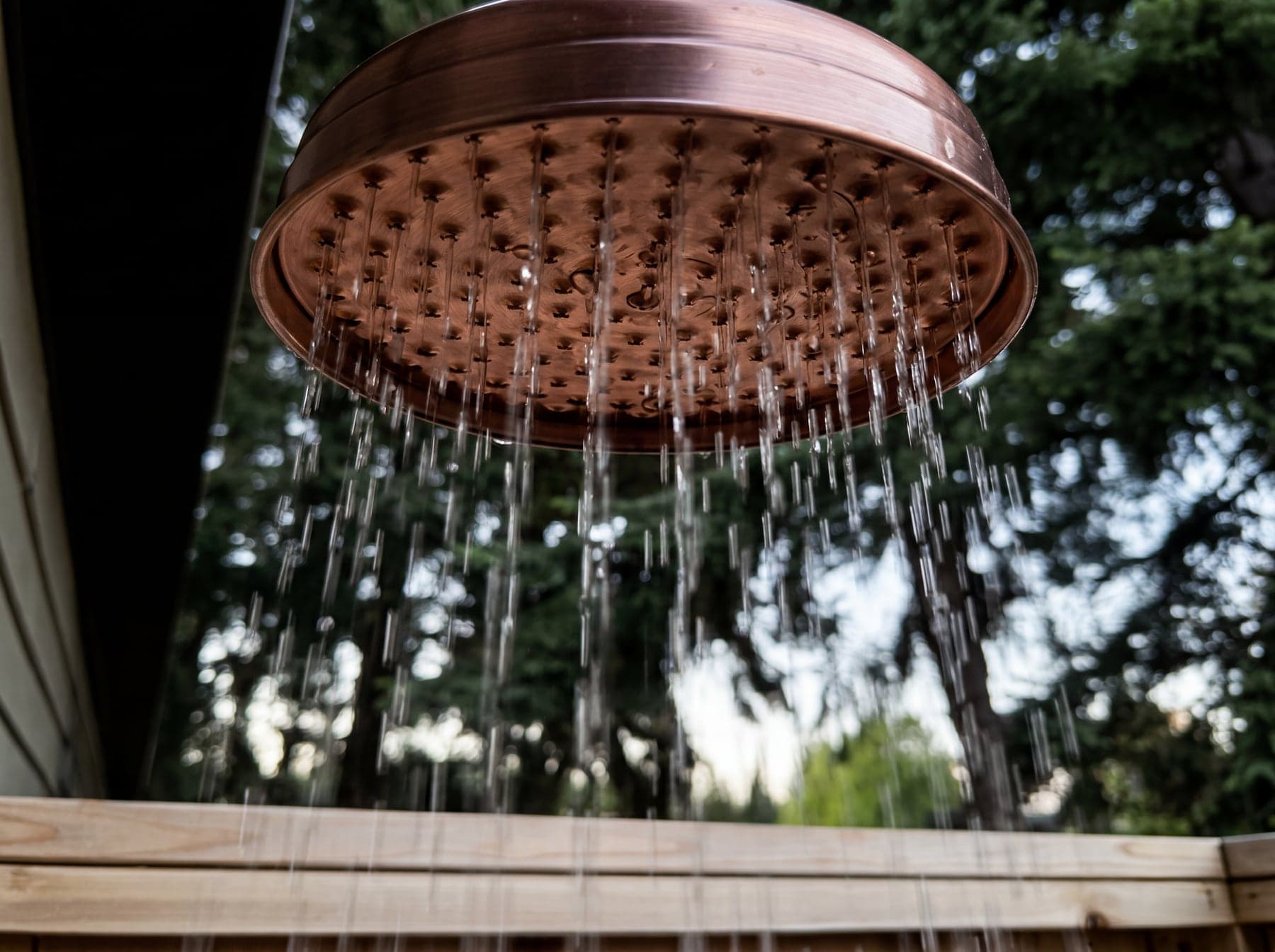 Water falling from the copper rain head with evergreen trees beyond the cedar walls